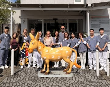 Group of students in scrubs posing with an orange horse statue in front of a building entrance.